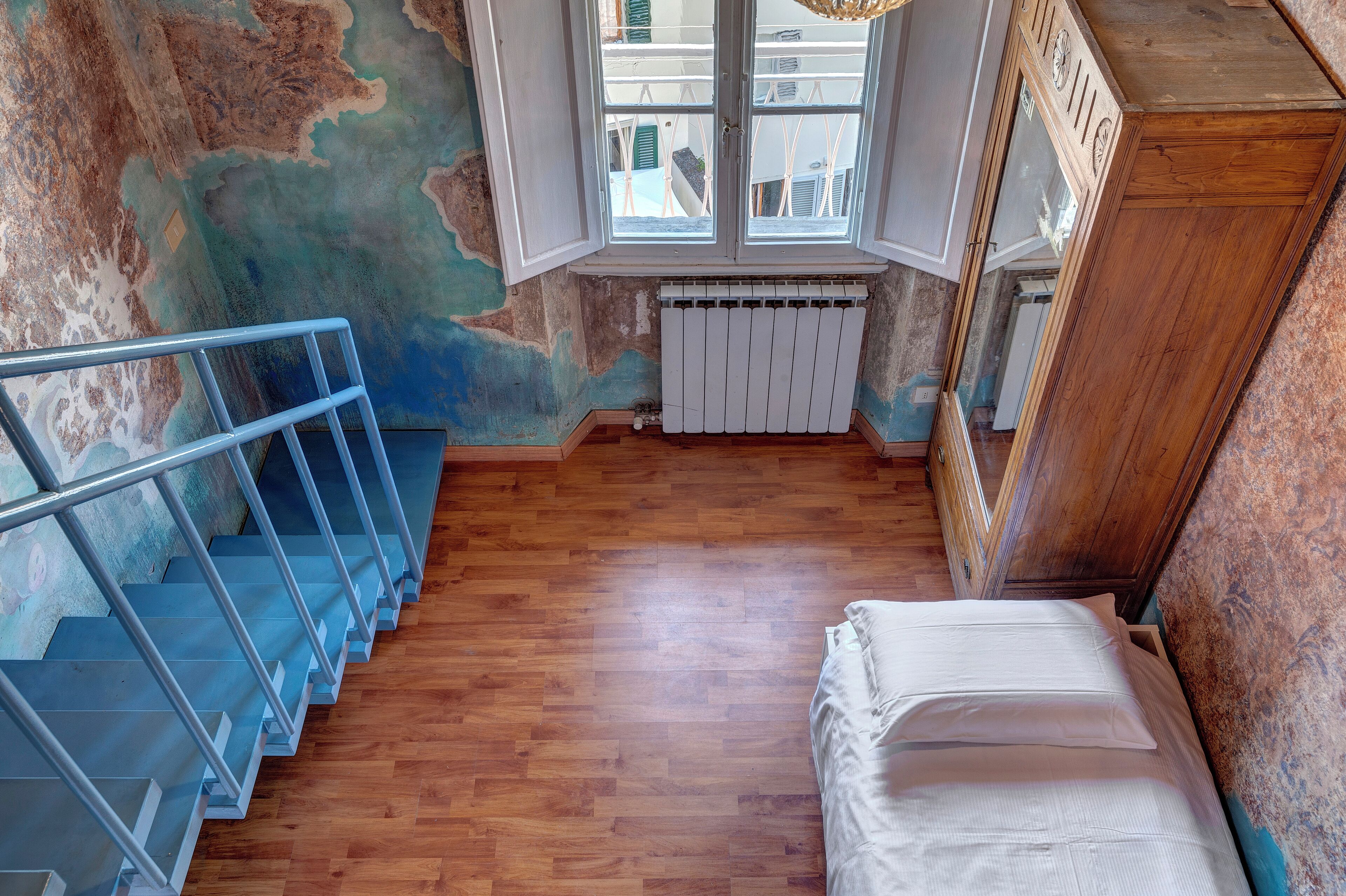 Une pièce avec un escalier en bois, un radiateur et un lit.
