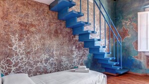 Ein Schlafzimmer mit einem Bett, einem Nachttisch und einer blauen Treppe an einer strukturierten Wand.