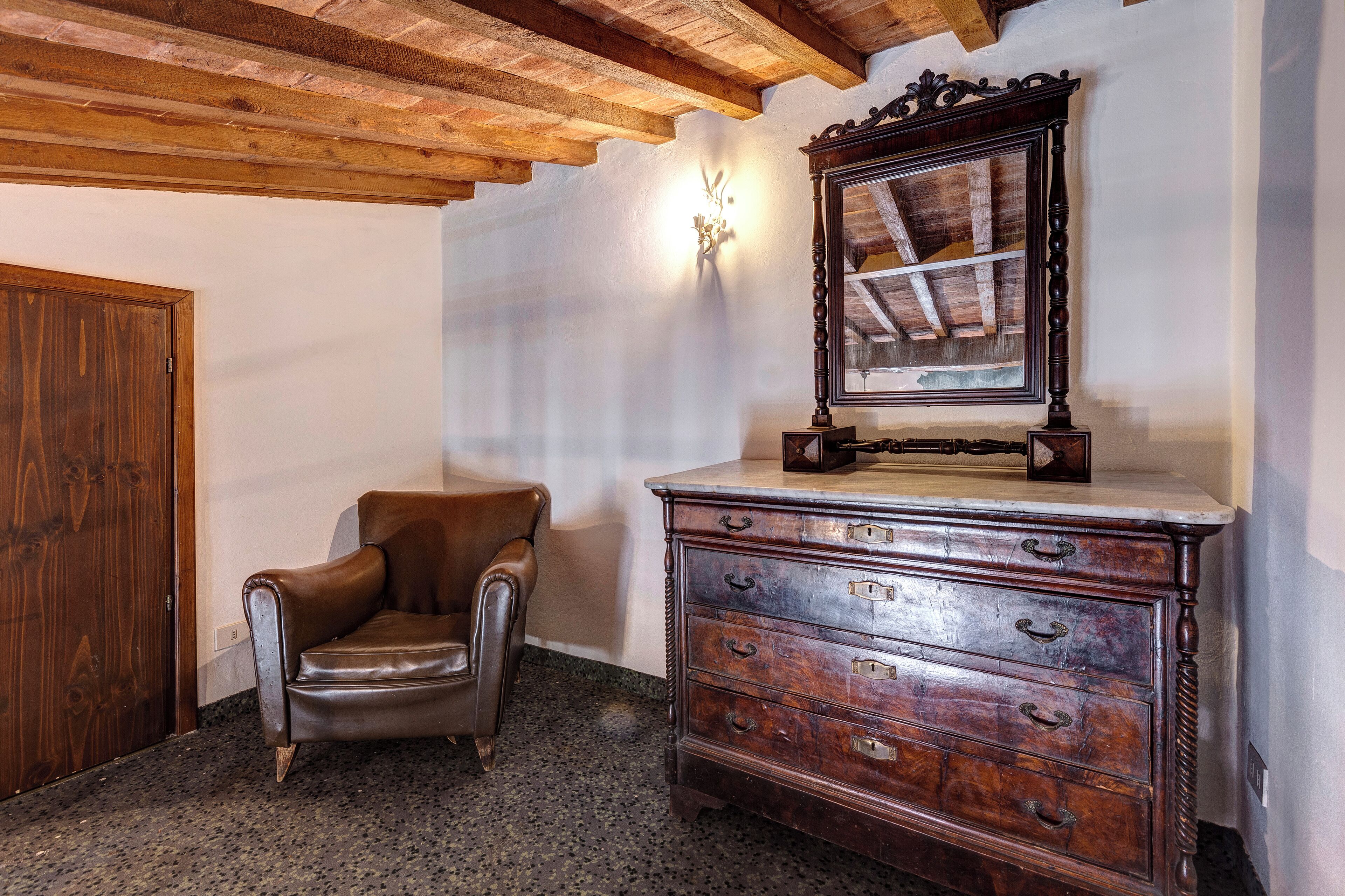 A room with a wooden ceiling, a brown leather chair, a wooden dresser with drawers, and a wall-mounted mirror.