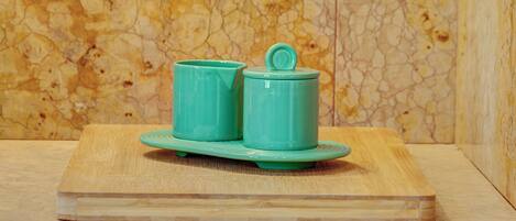 A wooden cutting board with a pair of teal ceramic cups and a lid on it.