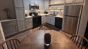 A modern kitchen with grey cabinets, a stainless steel refrigerator, a microwave, and a dining table with chairs. - IN TOWN CONDO WITH HOT TUB, AT SHUTTLE STOP, HAS EVERYTHING YOU NEED!! (Mammoth Lakes)