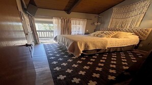 A bedroom with a large bed, a wooden ceiling, a patterned rug, and a view of the outdoors. - IN TOWN CONDO WITH HOT TUB, AT SHUTTLE STOP, HAS EVERYTHING YOU NEED!! (Mammoth Lakes)