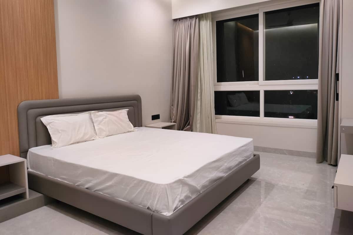 A modern bedroom with a large bed, a nightstand, a window with curtains, and a wooden panel on the wall.