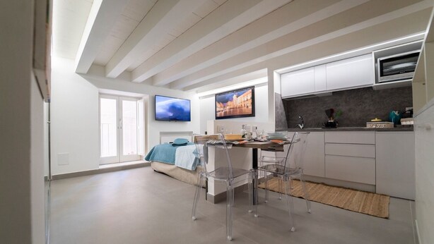 A modern kitchen with white cabinets, a built-in oven, and a dining area with a table and chairs. - Ortigia CLARME Cathedral Square (Siracusa)
