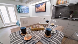A modern kitchen with a dining area, featuring a wooden table with striped placemats, black and white mugs, and a box of Dolce Gusto coffee. - Ortigia CLARME Cathedral Square (Siracusa)