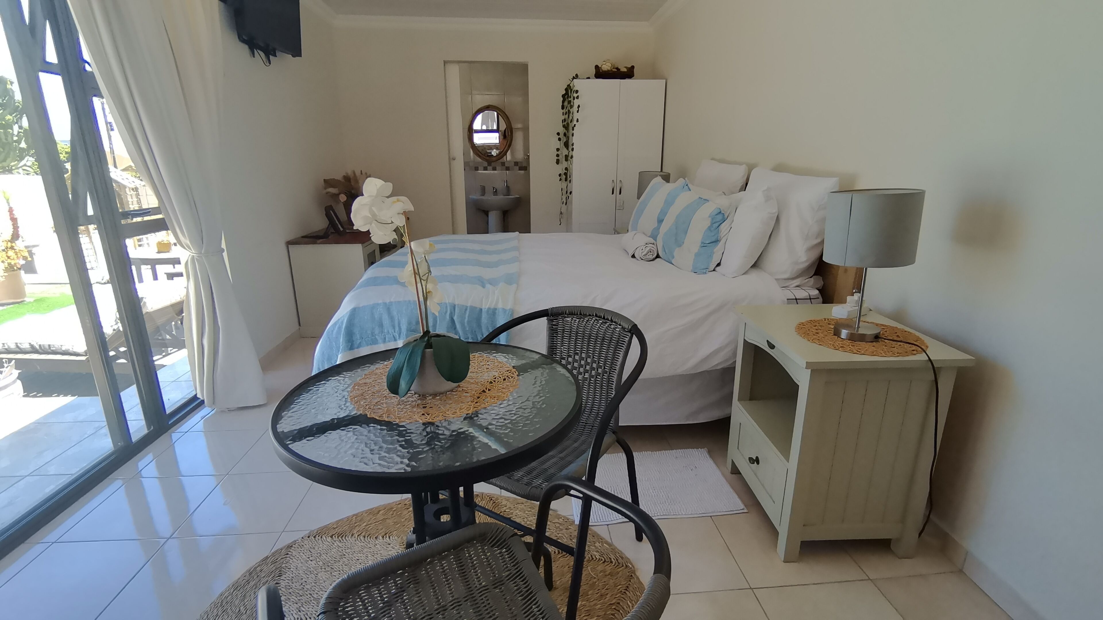 A bedroom with a bed, bedside table, lamp, and a view of the outside.
