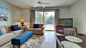 Ein Wohnzimmer mit Sofa, Hocker, Fernseher und Deckenventilator.