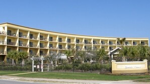 Ein mehrstöckiges Hotel mit Balkonen, einem Schild mit der Aufschrift 'Guest Services' und einem eingezäunten Bereich mit Palmen.