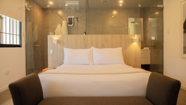 A modern hotel room with a large bed, a glass shower enclosure, and a wooden headboard. - Casa La Paz by Wynwood House (Lima)
