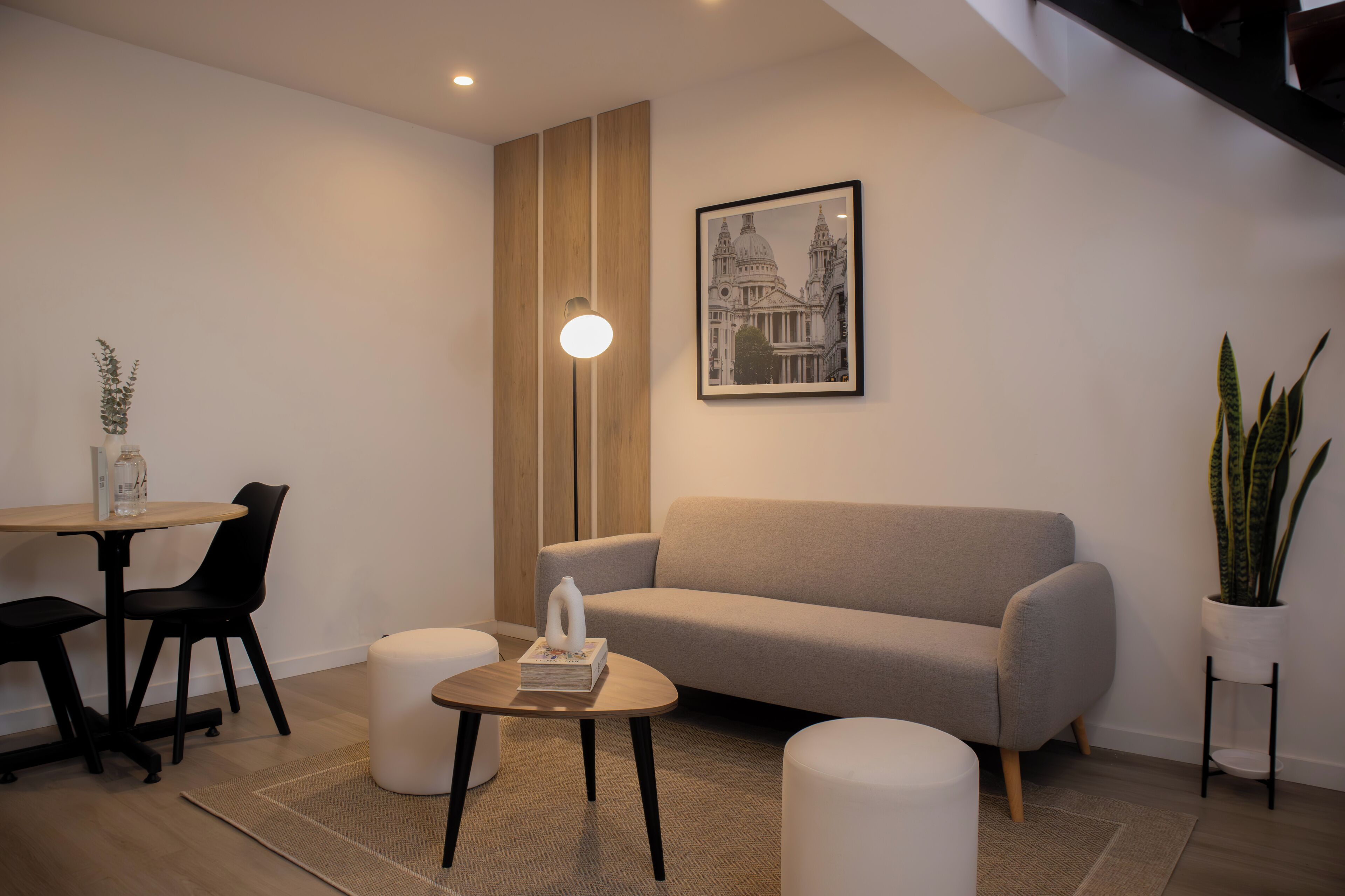 Una sala de estar moderna con un sofá, una mesa de centro, una mesa de comedor con sillas, una planta en maceta y un cuadro en la pared.