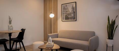 Una sala de estar moderna con un sofá, una mesa de centro, una mesa de comedor con sillas, una planta en maceta y un cuadro en la pared.