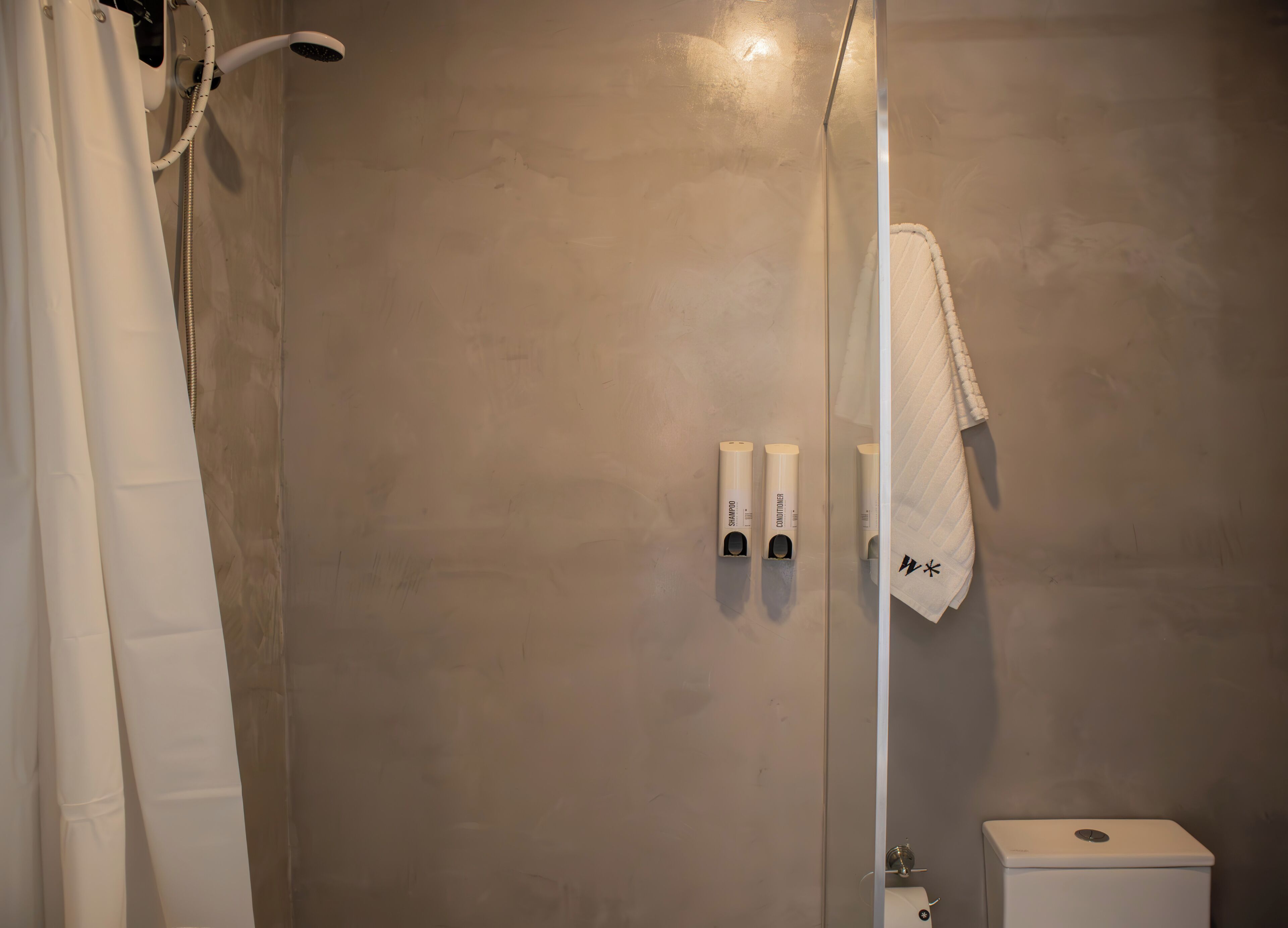 A bathroom with a shower, a toilet, and two shampoo and conditioner dispensers.
