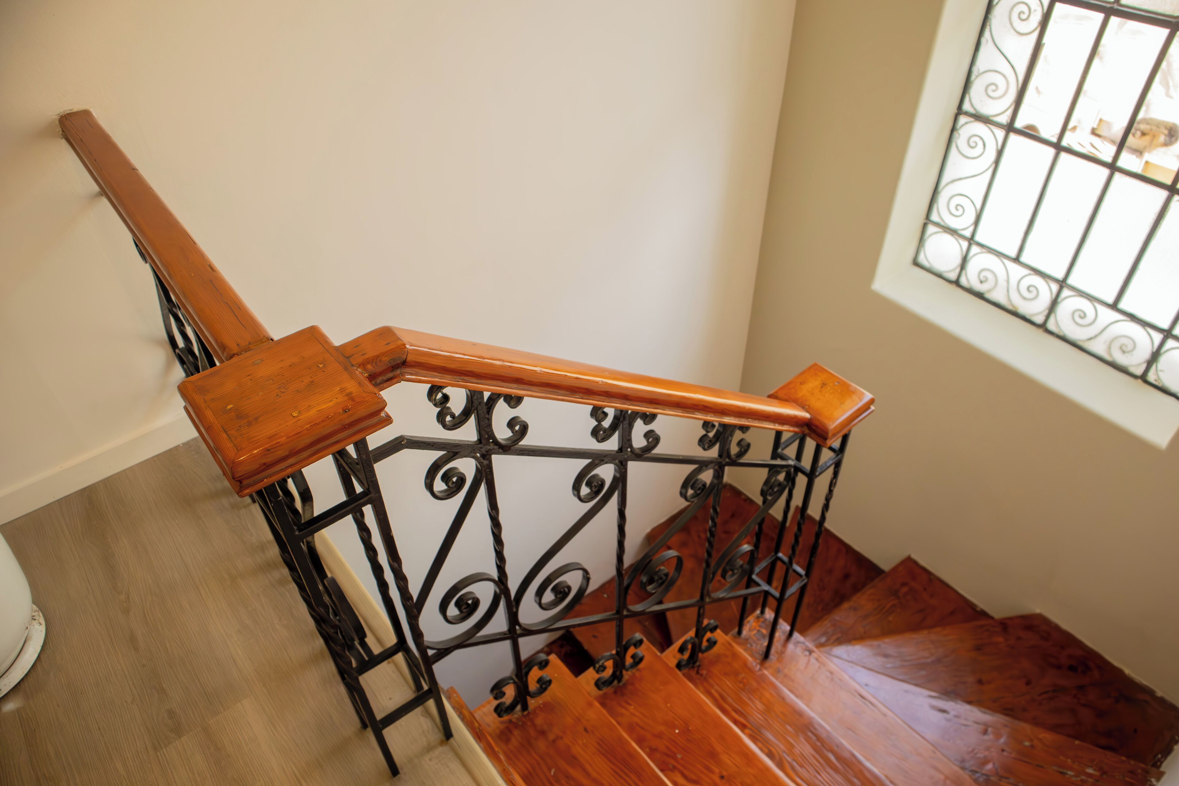 Uma escadaria de madeira com guarda-mão de metal e janela com grades decorativas.