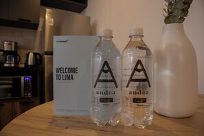 Dos botellas de agua con la marca 'andea' sobre una mesa de madera, un letrero de bienvenida y un jarrón blanco con una planta.