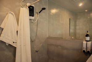 Un baño moderno con cabina de ducha, un perchero con toallas, un cabezal de ducha manual y dos botellas de champú y acondicionador.