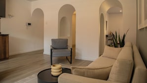 A modern living room with a beige sofa, a grey armchair, and a coffee table. There are three arched doorways leading to other rooms. - Casa La Paz by Wynwood House (Lima)