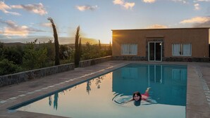 A swimming pool with a person in the water, surrounded by a stone deck and a building with a glass door. - Atlas Horizon Marrakech Auberge and Suites (marrakech)
