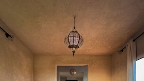 A room with a patterned rug, two sofas with patterned cushions, a hanging light fixture, and a view through an archway to another room with a fireplace. - Atlas Horizon Marrakech Auberge and Suites (marrakech)