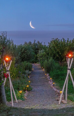 A pathway leading to a beach with a crescent moon in the sky, flanked by greenery and illuminated by small lanterns. - Atlas Horizon Marrakech Auberge and Suites (marrakech)
