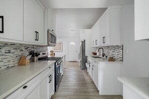 A modern kitchen with white cabinetry, a tiled backsplash, and a wooden floor.