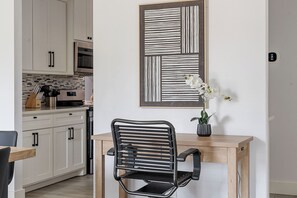A modern kitchen with white cabinets, a wooden dining table, a black chair, and a framed abstract artwork above the table. - 0.8 Mi to AT&T | Stadium View | Walk to Games (Arlington)