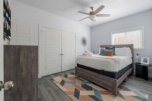 A bedroom with a bed, a ceiling fan, a window with blinds, and a door.