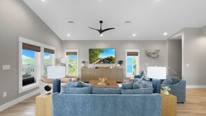 A modern living room with a large blue sofa, a wooden coffee table, and a dining area with a wooden cabinet. - Cape San Blas Gulf Views, Private Pool, Steps to Beach (Port St. Joe)