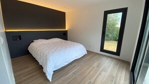 Un dormitori modern amb un llit, terres de fusta, una paret d'accent fosc i una finestra que dona a zona verda.