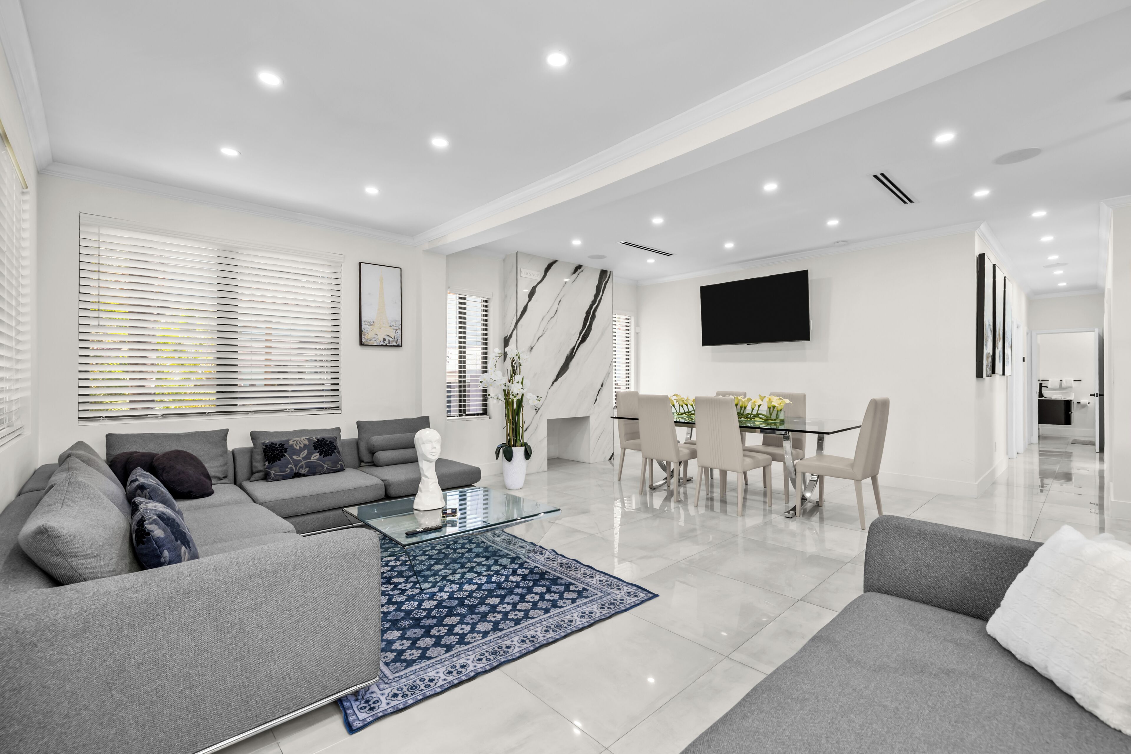 A modern living room with a grey sofa, a glass coffee table, and a dining area with a white table and chairs.