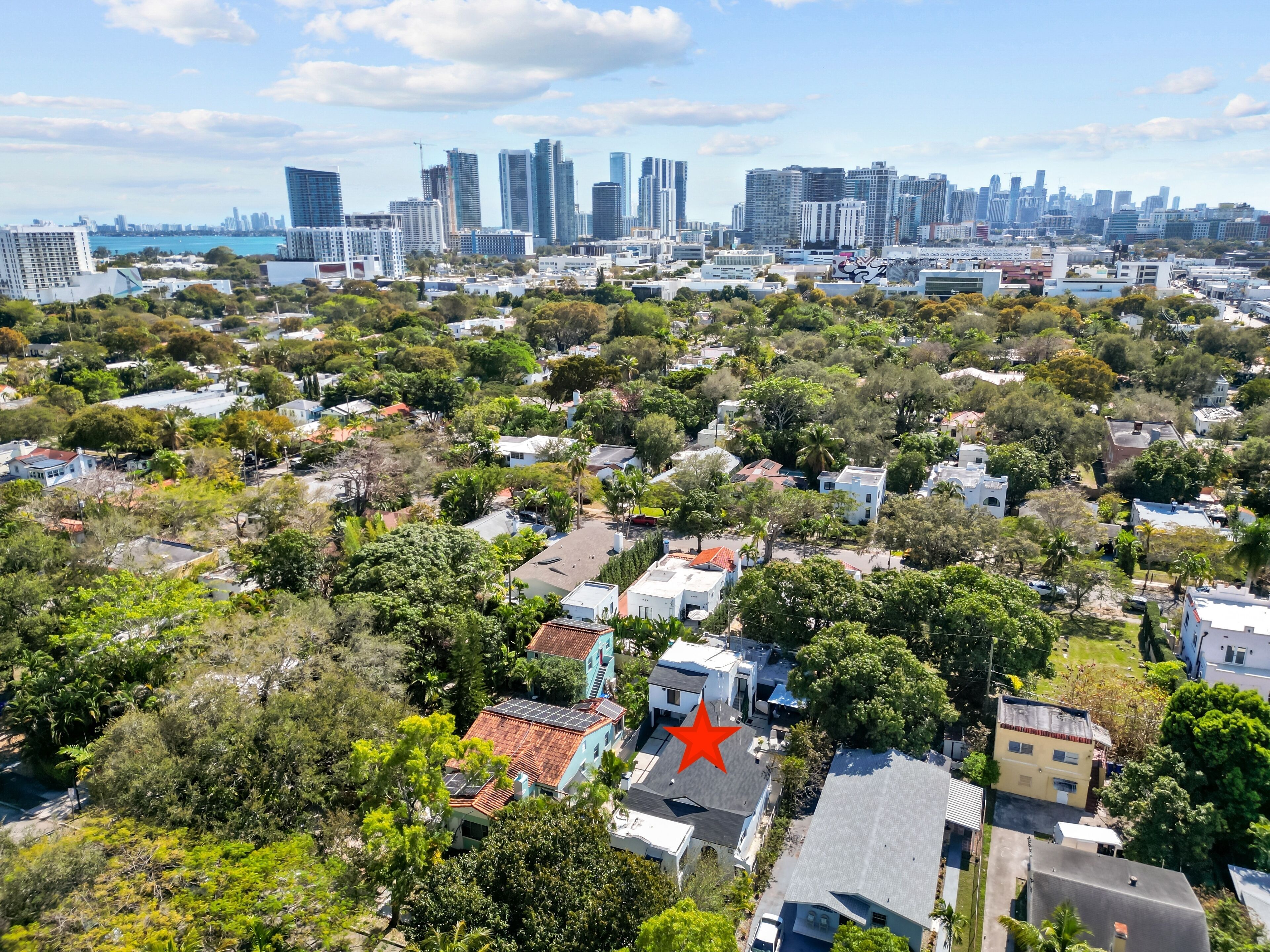 An aerial view of a residential area with a mix of single-family homes and apartment buildings, surrounded by greenery and a distant city skyline.