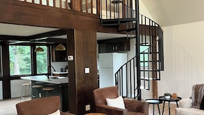 Un vaste espace de vie doté d’un haut plafond, d’un escalier en bois et d’une cuisine située au fond de la pièce.