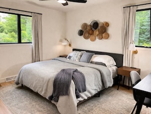 Une chambre à coucher comprenant un lit, des tables de chevet, un bureau et un ventilateur de plafond.