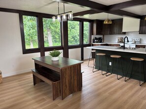Une cuisine moderne dotée d’un grand îlot central, de tabourets de bar et offrant une vue sur la verdure grâce à de grandes fenêtres.