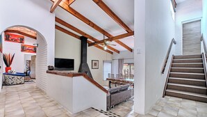A spacious living area with a high ceiling, wooden beams, a fireplace, and a staircase leading to another level.