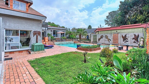 A residential backyard with a swimming pool, a patio area, and a variety of plants.