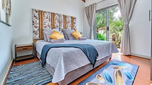 A bedroom with a bed, a nightstand, a large window with curtains, and a view of greenery outside.