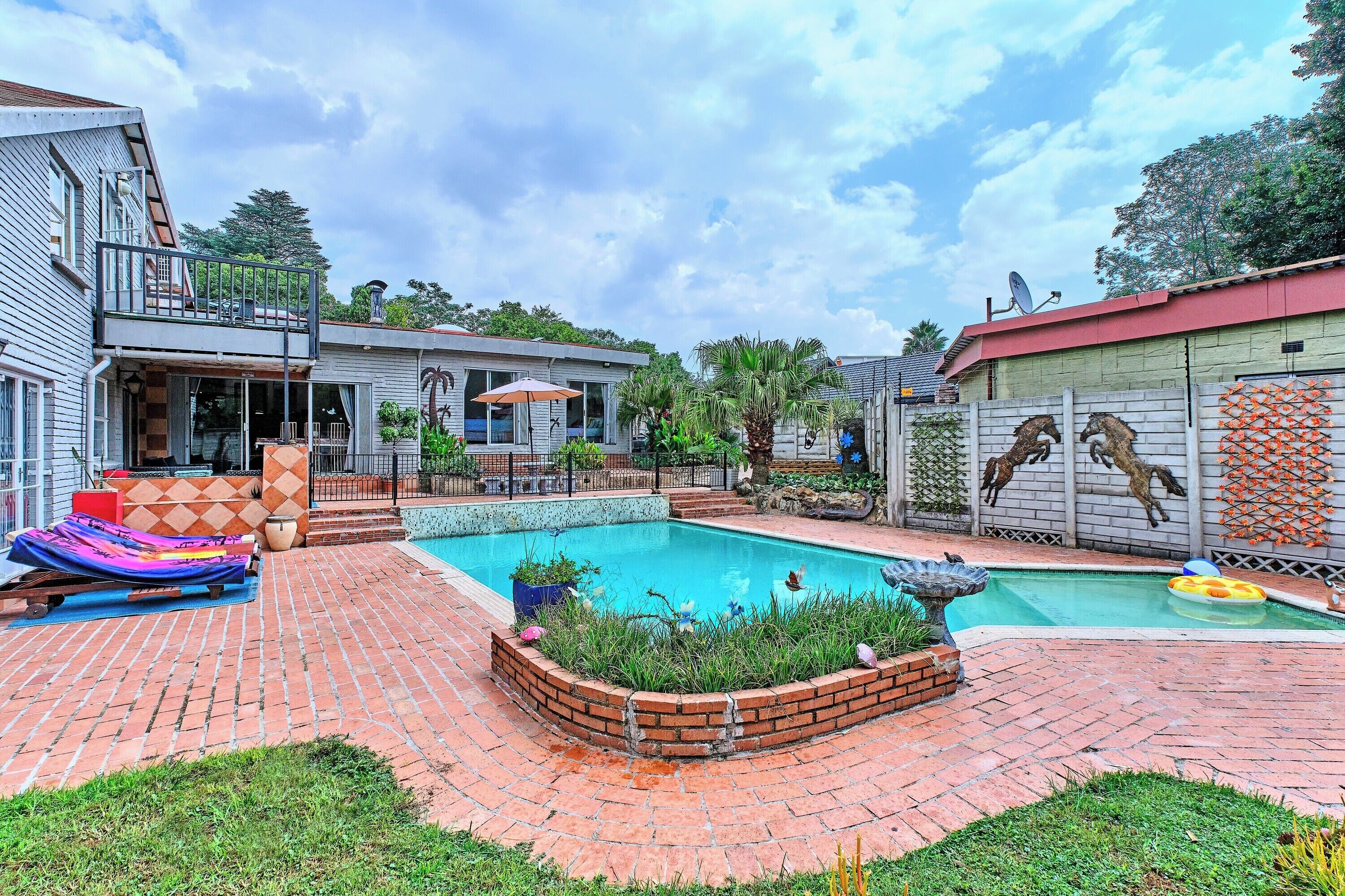 A backyard with a swimming pool, a barbecue area, and a fenced garden.