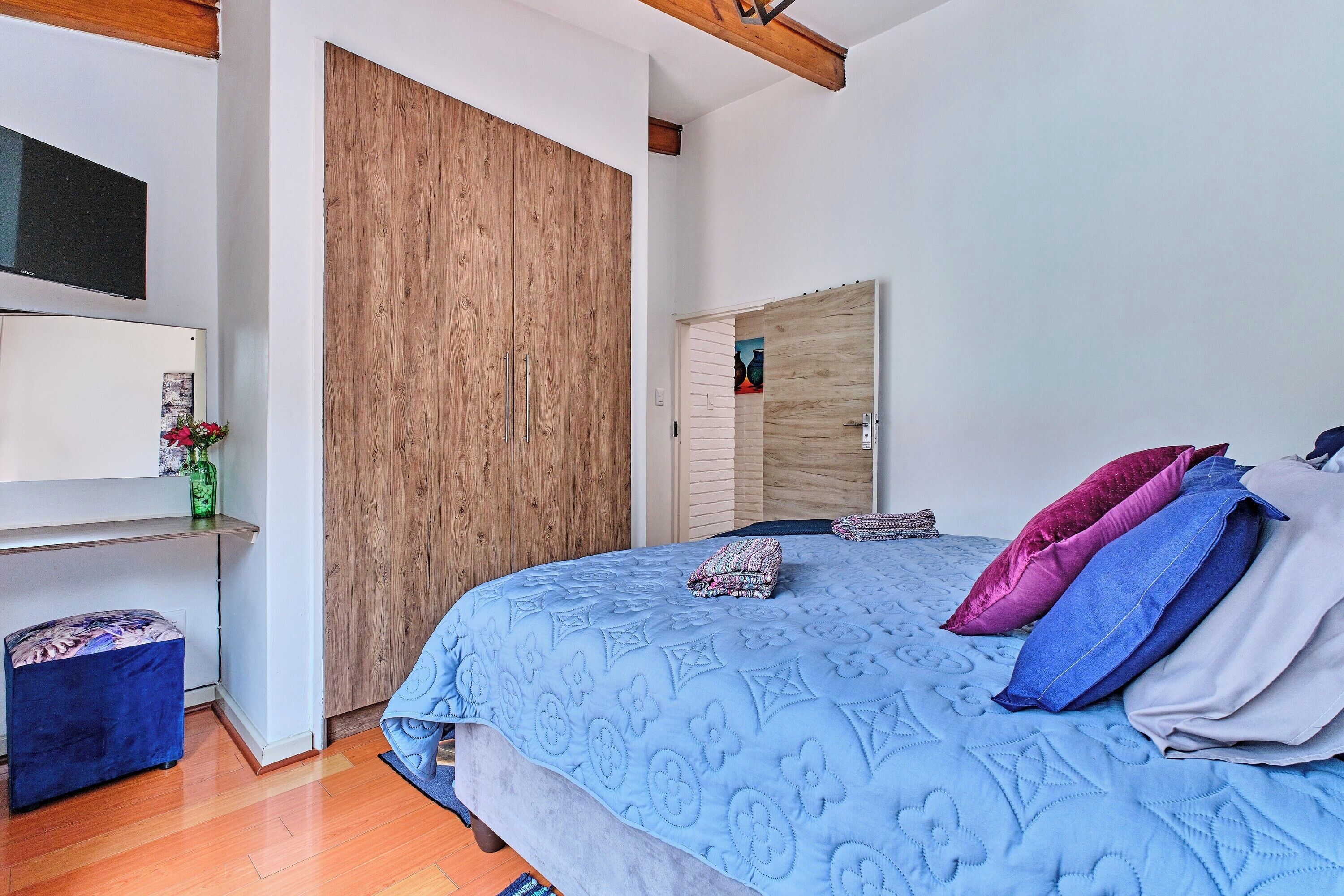 A bedroom with a large bed, wooden wardrobe, and a TV mounted on the wall.