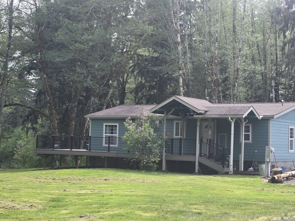 Una casa de dos pisos con un porche, rodeada de un bosque.