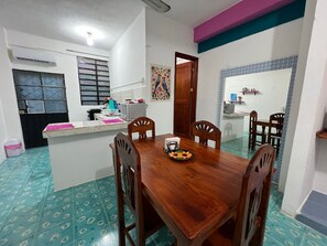 Un comedor con una mesa de madera y cuatro sillas, un área de cocina con microondas y pileta, y un cuadro decorativo en la pared.