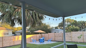 A covered patio area with a view of a backyard, featuring a wooden fence, a lawn, and a string of lights. - Dogs Welcome-Close to Beach-Fenced Yard (Sebastian)