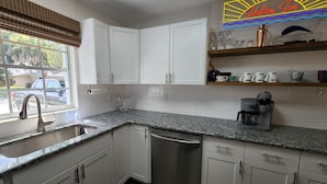 A modern kitchen with white cabinets, a granite countertop, a coffee maker, and a neon sign above the counter. - Dogs Welcome-Close to Beach-Fenced Yard (Sebastian)