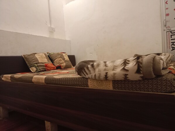 A bed with a patterned blanket and pillows, a wooden headboard, and a white wall with a sign.