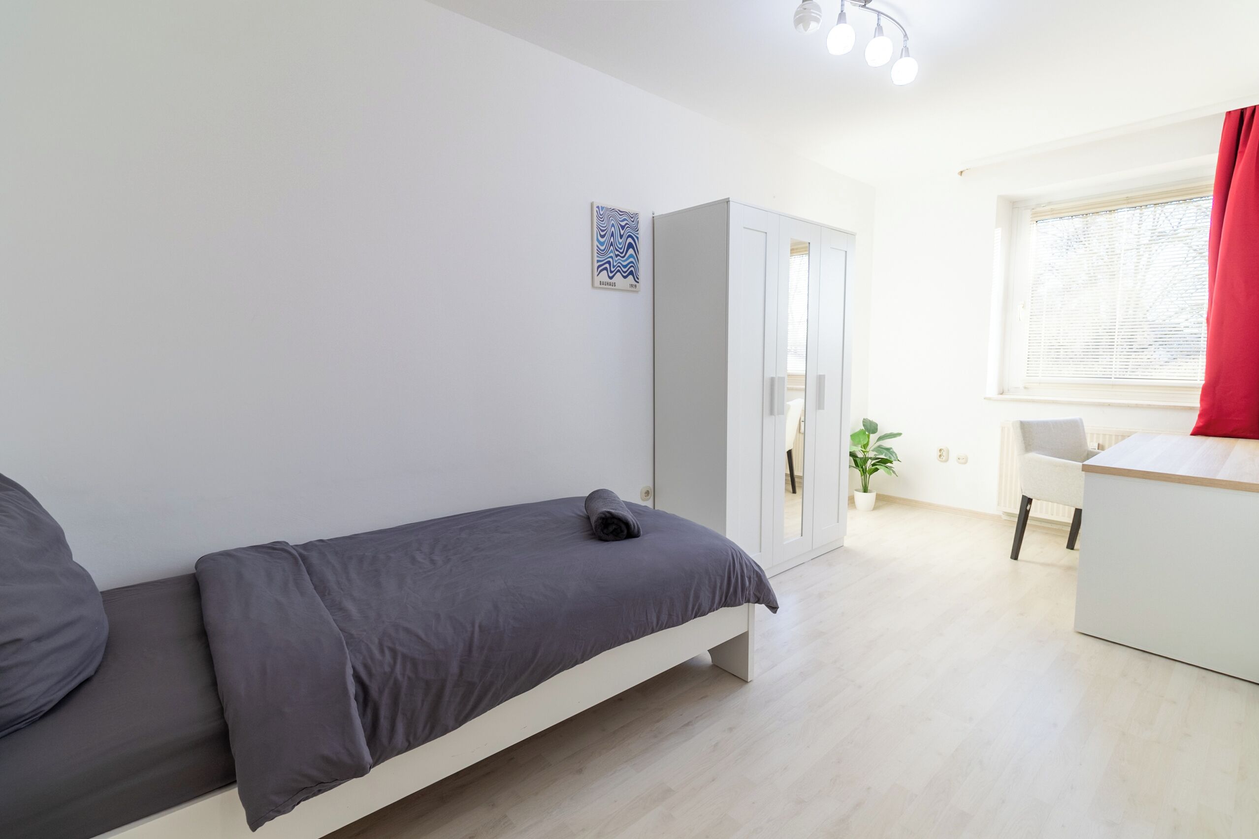 A minimalist room with a bed, a wardrobe, a desk, and a window with curtains.