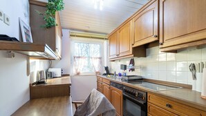 A compact kitchen with wooden cabinets, a built-in oven, and a window with curtains. - Bright, central 4-room apartment in Braunschweig (Braunschweig)