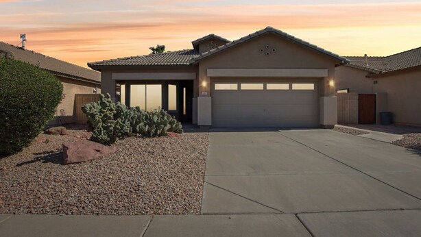A residential house with a garage, a covered driveway, and a desert landscape with cacti. - Cozy 3 bedroom home with private heated pool on a golf course with mountain view (Avondale)