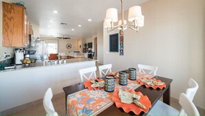 A dining area with a table set for four, a chandelier, and a kitchen in the background. - Cozy 3 bedroom home with private heated pool on a golf course with mountain view (Avondale)