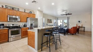 A spacious kitchen with wooden cabinets, stainless steel appliances, and a central island with bar stools. - Cozy 3 bedroom home with private heated pool on a golf course with mountain view (Avondale)