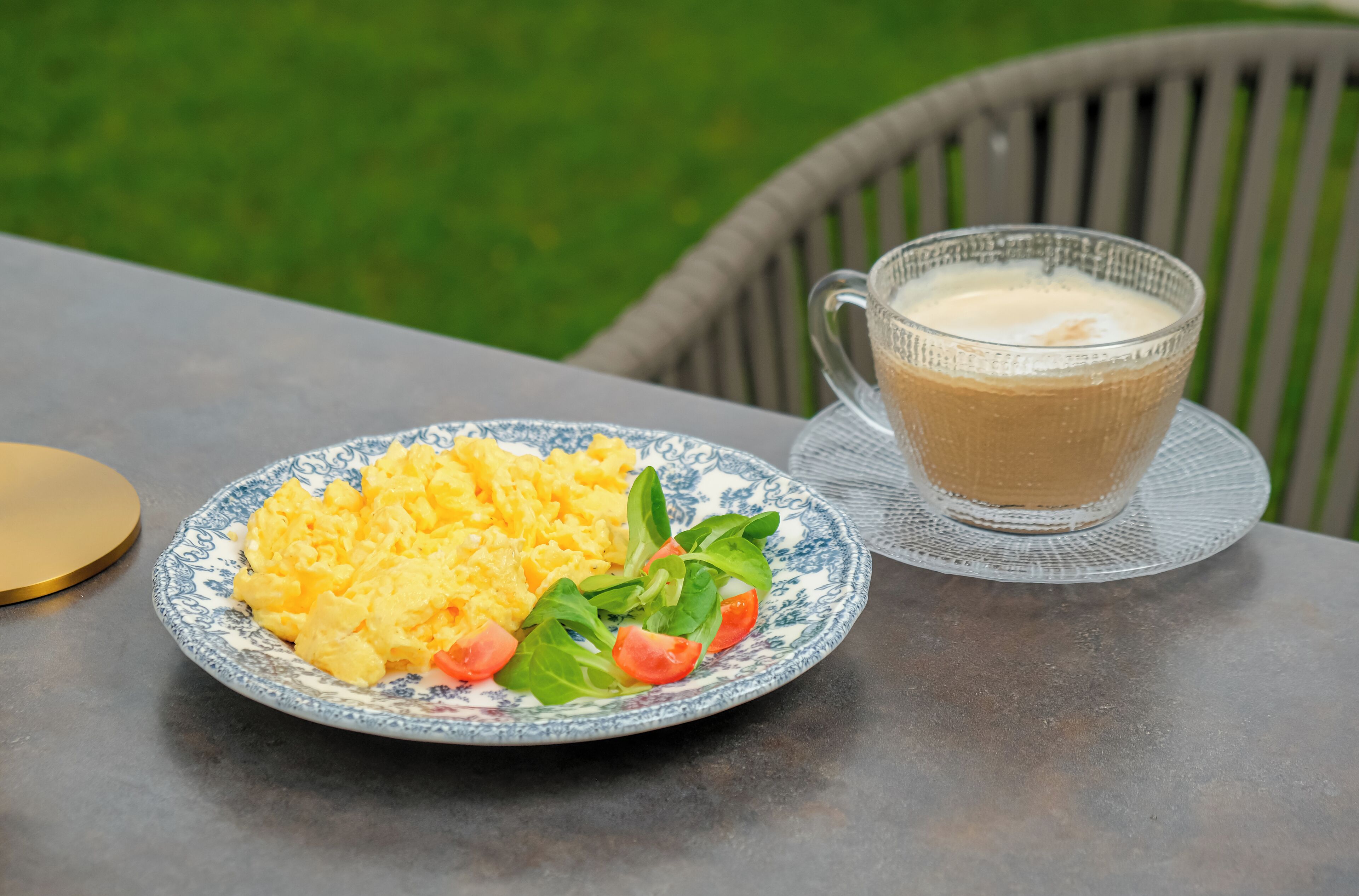 Un plato de huevos revueltos con espinacas y una taza de café sobre una mesa al aire libre.