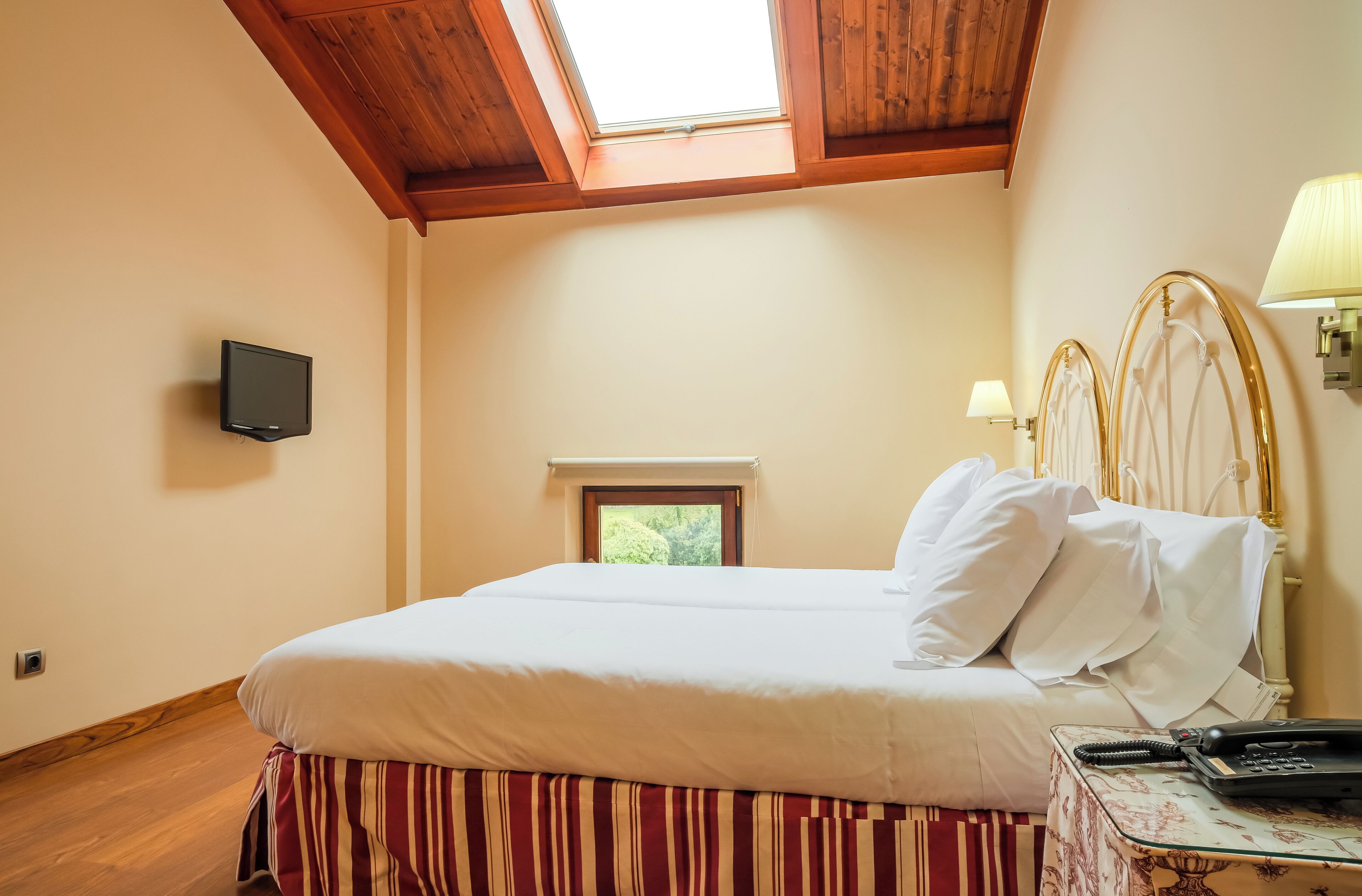 Un dormitorio con techo de madera, una cama con ropa de cama blanca, una mesita de noche con lámpara y un televisor en la pared.